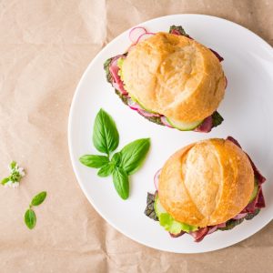 Ready-to-eat hamburgers with pastrami, vegetables and basil on a plate on craft paper.