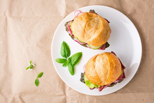 Ready-to-eat hamburgers with pastrami, vegetables and basil on a plate on craft paper.